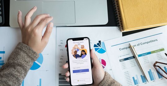 Eine Angestellte lädt auf ihrem Handy die Microsoft Teams App für digitale Zusammenarbeit herunter.