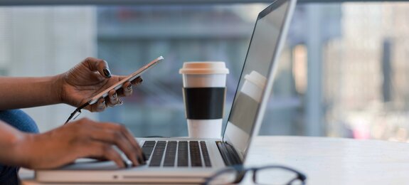 Frau arbeitet remote mit Smartphone und Laptop