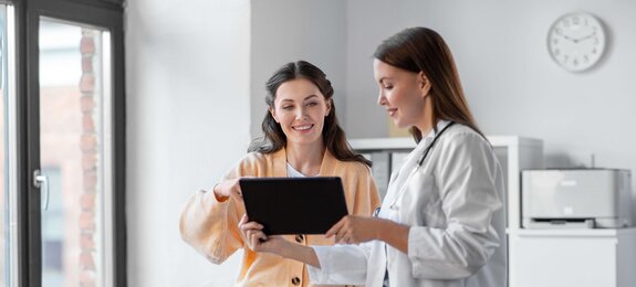 medicine, healthcare and people concept - female doctor with tablet pc computer talking to smiling woman patient at hospital