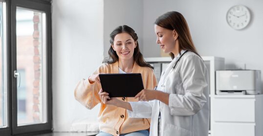 medicine, healthcare and people concept - female doctor with tablet pc computer talking to smiling woman patient at hospital