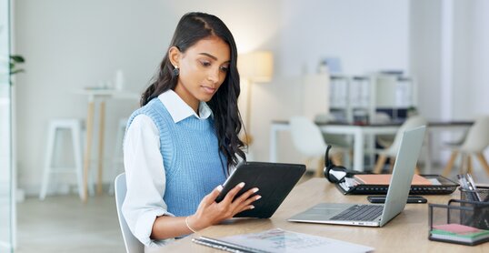 Trendy marketing professional using an online app to network, meet deadlines and stay connected during office hours. Young business woman using her laptop and tablet while working in the office.