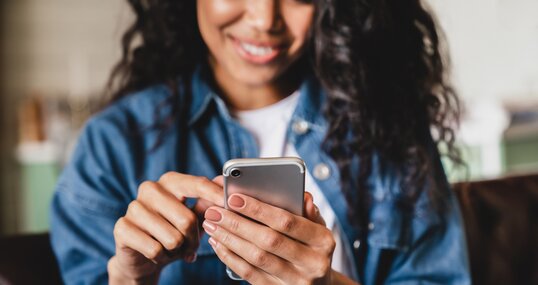 Cropped shot of an african-american young woman using smart phone at home. Smiling african american woman using smartphone at home, messaging or browsing social networks while relaxing on couch