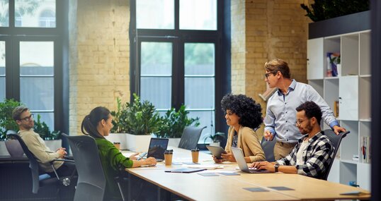 Office life. Group of young multiracial people sitting at the table in coworking space and working together, using modern technologies and discussing project