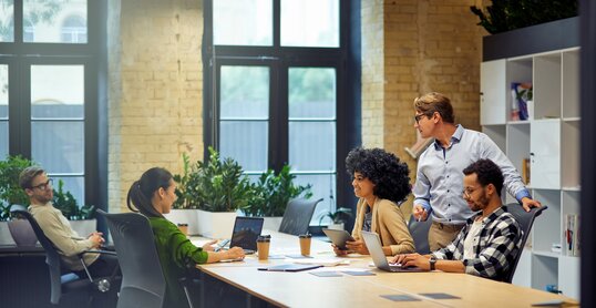 Office life. Group of young multiracial people sitting at the table in coworking space and working together, using modern technologies and discussing project