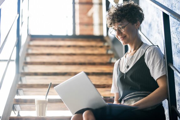 Pretty designer in casualwear sitting on staircase with laptop on her knees