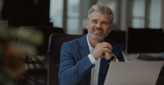 Smiling Mature businessman working on laptop while sitting in modern coworking