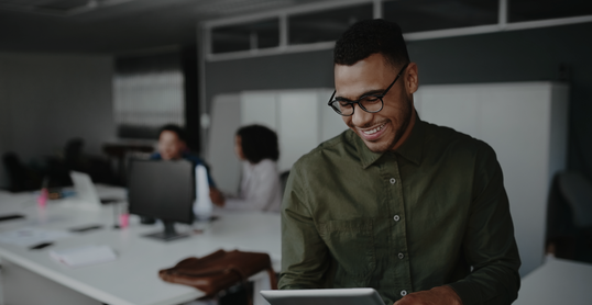 Cheerful young businessman using digital tablet smiling while his colleagues working at the background