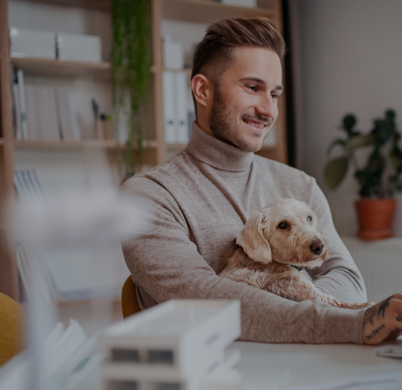 Young businessman with dog sitting at the desk indoors in office, using computer.