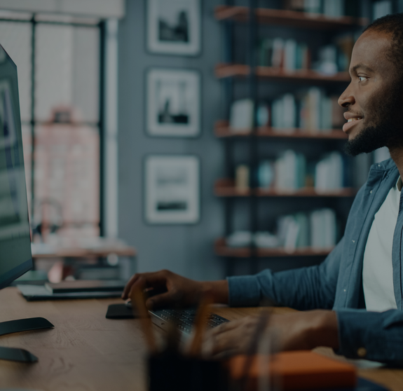 Handsome Black African American Specialist Working on Desktop Computer in Creative Home Living Room. Freelance Male is Working on a Finance Presentation Report for Clients and Employer