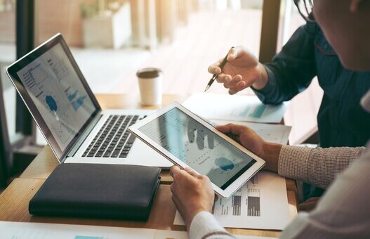 Business partnership coworkers using a tablet to chart company financial statements report and profits work progress and planning in office room.