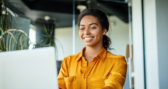 Happy black businesswoman using laptop typing and working online while sitting at workplace in office, copy space