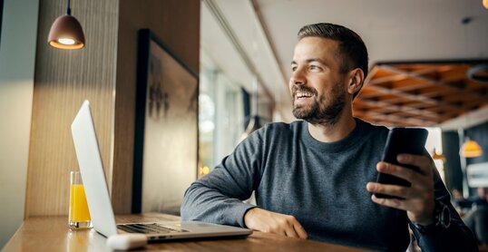 A happy casual entrepreneur is sitting in coffee shop and working on e-commerce by using cutting edge technologies.