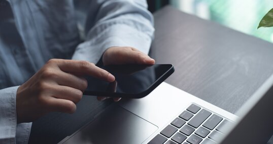 Closeup of woman finger touching on mobile phone screen. Asian woman using smartphone while sitting at table with laptop computer at home office, online shopping, mobile banking, internet payment