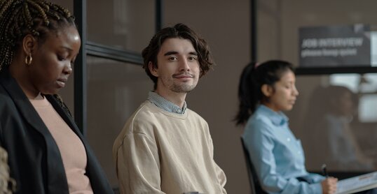 Portrait of young candidate sitting in waiting room with resume and looking at camera