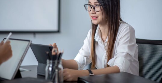 Junge Frau sitzt an Tisch und arbeitet mit Tablet