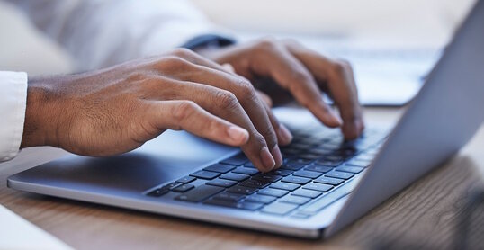 Laptop, office and hands typing at desk for online documents, writing email and business proposal. Technology, networking and zoom of businessman on computer for research, report and website review