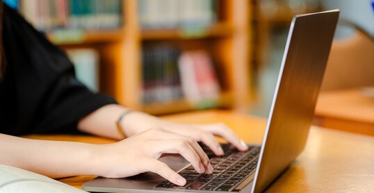 Female student using laptop on desk at library