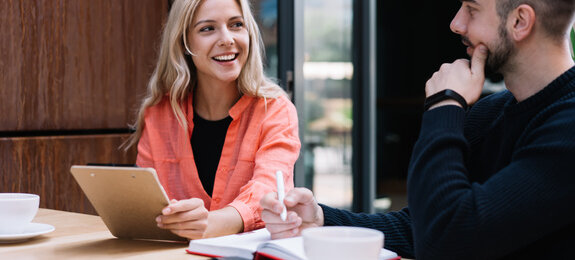 Cheerful caucasian female student looking a her male friend discussing learning project on cafe break, prosperous young man and woman employees talking to each other about business ideas on meeting