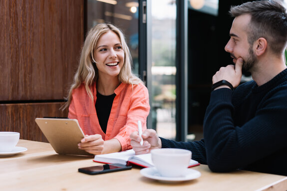 Cheerful caucasian female student looking a her male friend discussing learning project on cafe break, prosperous young man and woman employees talking to each other about business ideas on meeting