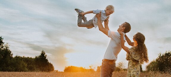 Fröhliche Familie mit Kind auf einem Feld beim Sonnenuntergrang