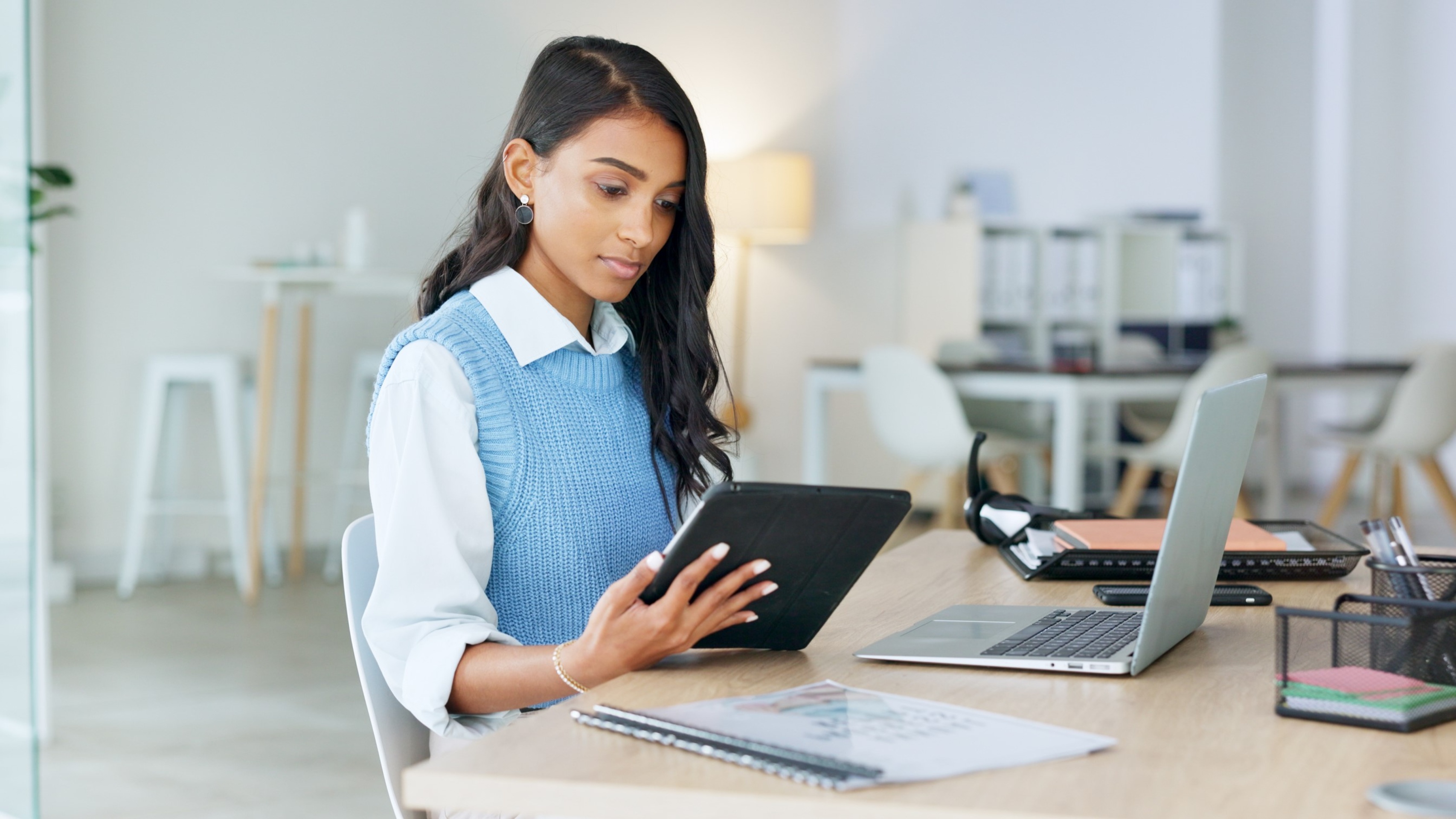 Trendy marketing professional using an online app to network, meet deadlines and stay connected during office hours. Young business woman using her laptop and tablet while working in the office.
